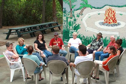 outdoor group therapy session with men and women sitting in front of campfire mural