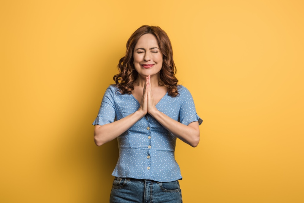 anxious-girl-showing-praying-hands-with-closed-eyes-on-yellow-background